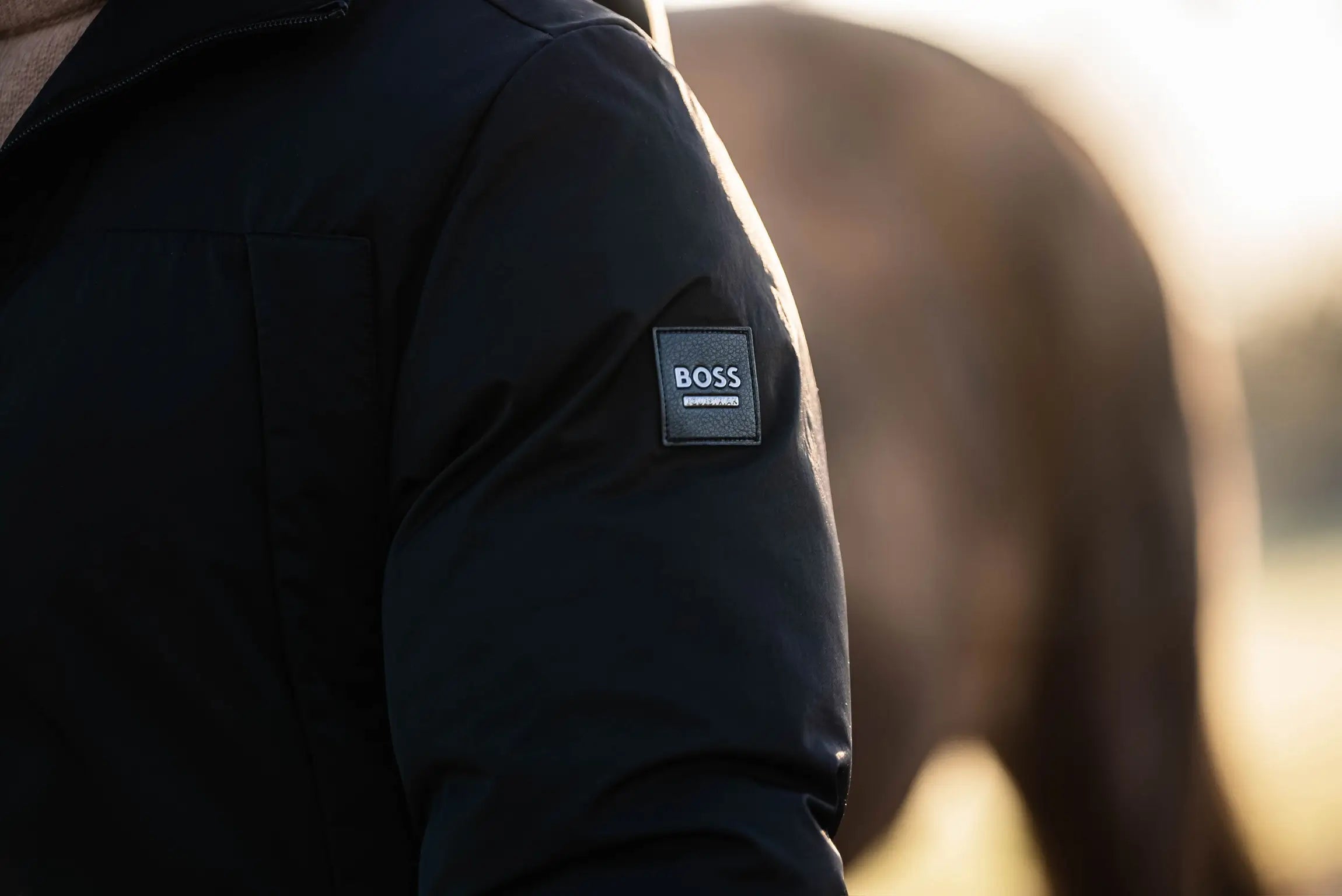 Black jacket with a BOSS logo on the sleeve against a blurred background
