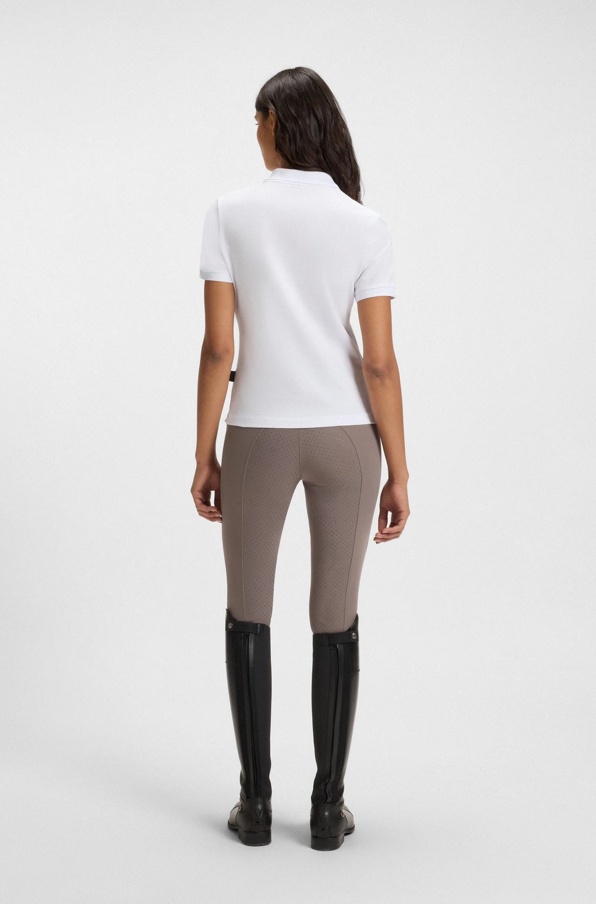 White | Person wearing a white shirt, beige leggings, and black riding boots on a white background