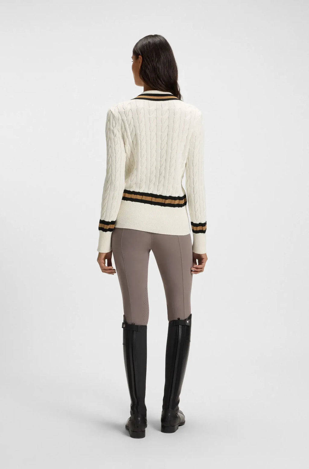 Soft Creme | Person wearing a white sweater with black and gold stripes, gray leggings, and black knee-high boots on a white background